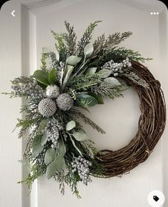 a wreath is hanging on the front door with greenery and pineconis around it