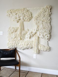 a black chair sitting in front of a wall hanging with tassels on it