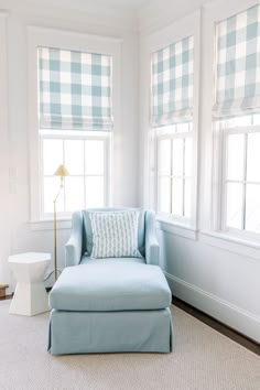 a blue chair and ottoman in front of two windows with checkered shades on them