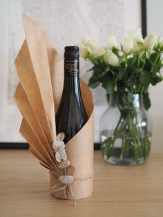 a wine bottle wrapped in brown paper next to a vase with white flowers