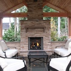 two chairs and a table sitting in front of a fire place under a wooden roof