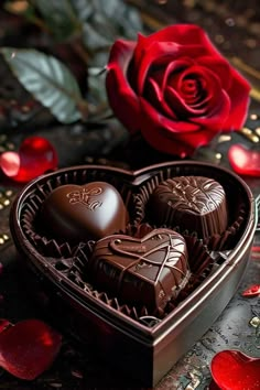 two chocolates in a heart shaped box next to a red rose and petals on a table