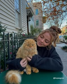 a woman petting an orange cat on top of a green table in front of a house