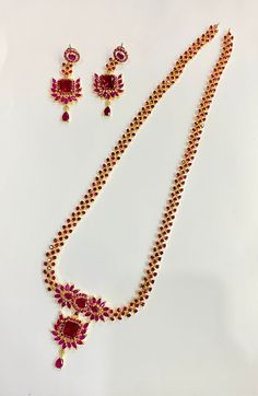 **Elegant Ruby Floral Necklace Set** - **Polish 22k Gold Plated, providing a rich and luxurious finish that enhances the vibrant red stones. - **Stones Beautiful ruby-colored simulated stones are arranged in a floral pattern, creating a delicate and elegant look. - **Design The necklace features intricate detailing with ruby stones set in a floral and geometrical pattern, along with matching earrings that complete the set. The design is perfect for special occasions and traditional events. - **Style Indian Traditional Jewelry - Perfect for weddings, festive events, and formal functions. - **Dimensions    - **Necklace Length 12 inches (plus an adjustable back chain).   - **Earring Length 6 cm. - **Handmade Crafted with precision, this set is a piece of fine artisan work, featuring hand-set Red Ruby Temple Necklace For Celebration, Traditional Red Jewelry Sets With Stones, Red Gold-plated Jewelry Set For Wedding, Festive Red Ruby Necklace, Celebration Ruby Jewelry Sets With Stone Work, Ruby Jewelry Sets With Stone Work For Celebration, Red Temple Necklace With Hand-set Detail As Gift, Elegant Red Necklace With Stone Setting, Red Ruby Stone Setting Necklace