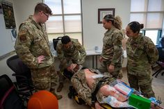 four soldiers are doing medical tasks in an office setting with one laying on the floor