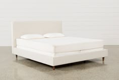 a white bed with two pillows on top of the headboard and foot board, in front of a white wall