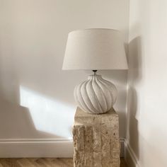 a lamp sitting on top of a stone block next to a white wall and wooden floor