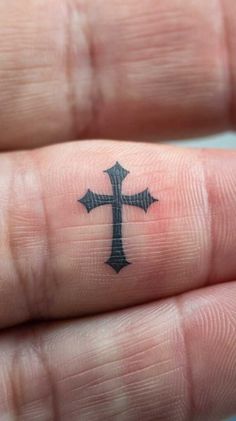 a small cross tattoo on someone's finger