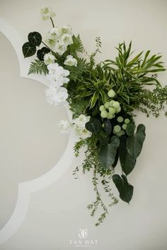 white flowers and greenery are arranged on the wall in front of a circular frame