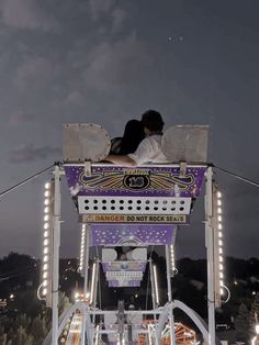 two people sitting on top of a carnival ride at night with the sky in the background