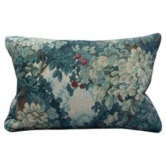 a blue and green floral pillow with red berries on the tree in the center, against a white background