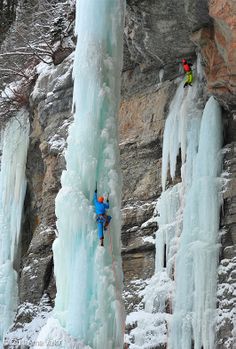 two climbers climbing up the side of an ice - covered cliff face each other