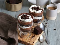 two desserts are sitting on a wooden board with spoons and cups in the background