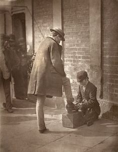 an old black and white photo of a man sitting on the ground next to a suitcase