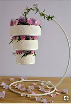 three tiered wedding cake with flowers on top, hanging from a white metal stand