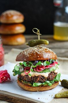 a hamburger with lettuce, tomato and pickles on it sitting on a cutting board