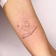 a woman's arm with a book and flowers tattoo on it