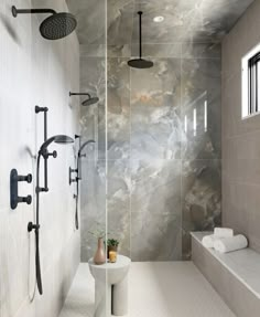 a bathroom with marble walls and flooring next to a bathtub, shower head, and window