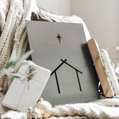 a canvas with a house and star on it sitting next to christmas presents in front of a window