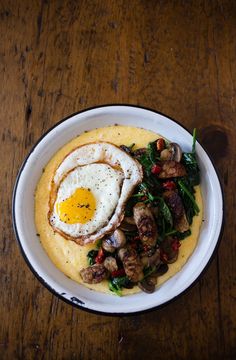 a white plate topped with an egg on top of polenta next to a fork