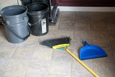 two buckets and a broom on the floor in front of some trash can's