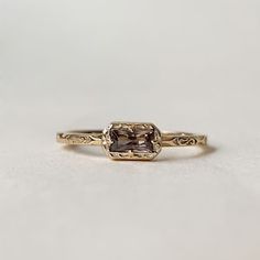 a gold ring with a brown diamond in it on a white surface and the band has an intricate design