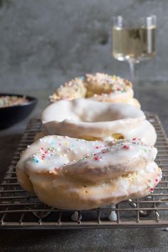 three glazed donuts with sprinkles and a glass of wine in the background