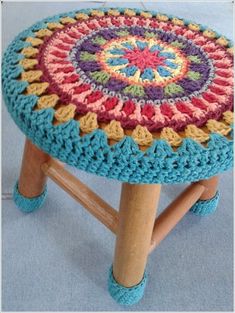 a crocheted stool with wooden legs and a colorful circular design on the top