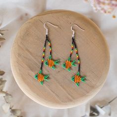 a pair of earrings with beads on top of a wooden table next to flowers and leaves