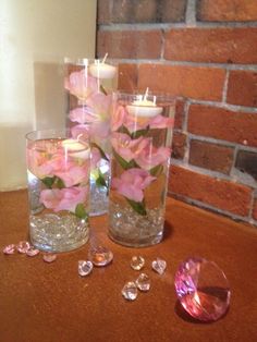 three glass vases with pink flowers in them on a table next to a candle