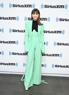 a woman standing in front of a wall wearing a green suit and black top with her hands on her hips