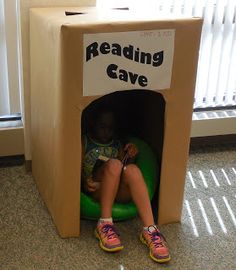 a child sitting in a reading cave made out of cardboard boxes with the words reading cave written on it