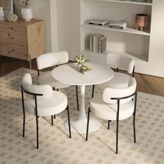 a white table with four chairs and a vase on top of it in front of a bookshelf