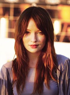 a woman with long red hair standing in front of a building and looking at the camera