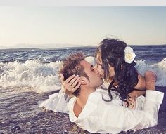 a man and woman kissing on the beach with waves crashing in front of their heads