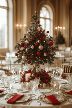 a decorated christmas tree sits on top of a round table with red napkins and place settings