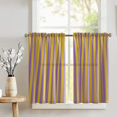 a yellow and purple striped curtain hanging in front of a window with a vase filled with flowers