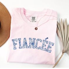 a pink t - shirt with the word fance on it next to a hat