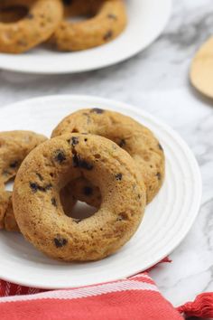 three chocolate chip donuts on a white plate with red and white napkins next to them