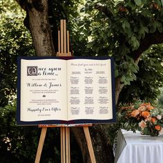 an open book sitting on top of a easel next to a table with flowers