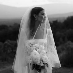 a woman in a wedding dress and veil is holding a bouquet with flowers on it