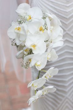 a bouquet of white orchids and baby's breath in a bridal gown