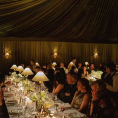 a large group of people sitting at tables in a room with candles on the table