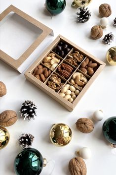 an assortment of nuts in a wooden box surrounded by christmas decorations and ornaments on a white surface