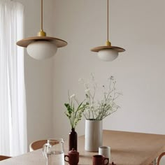 two pendant lights hanging over a table with vases and cups on top of it