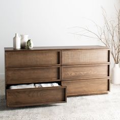 a large wooden dresser with drawers and vases on top of it in front of a white wall