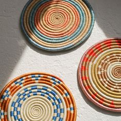 three woven baskets are arranged on the wall, one is multicolored and the other has circles