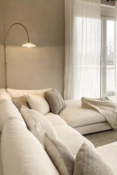 a large white couch sitting in front of a window next to a wall mounted lamp