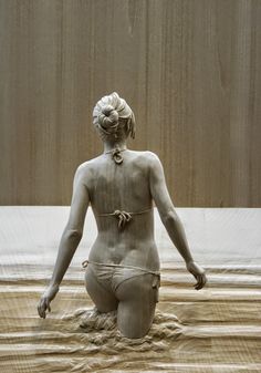 a statue of a woman sitting on top of a sandy beach next to a wooden wall