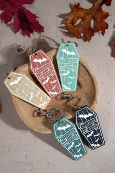 four keychains with different designs on them sitting on a wooden plate next to leaves